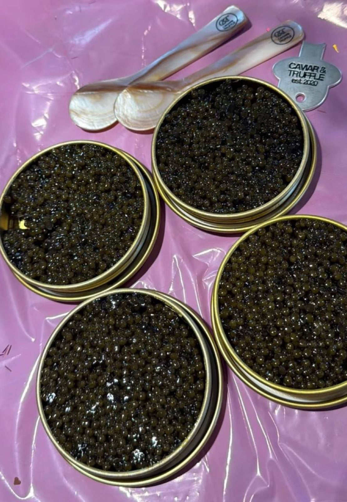 Four open tins of caviar with mother of pearl spoons and a branded opening key