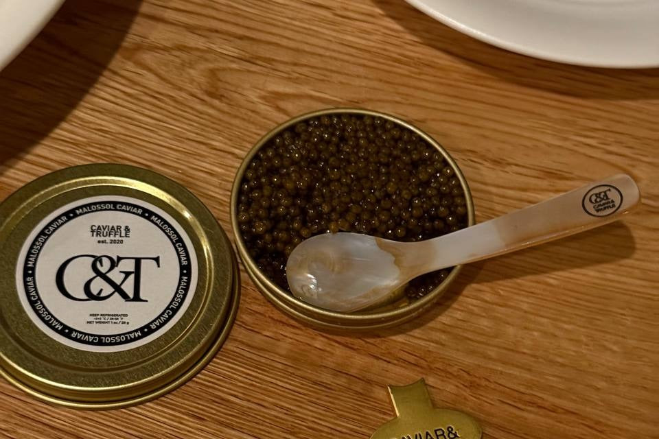 Open tin of caviar with mother of pearl spoons and branded key