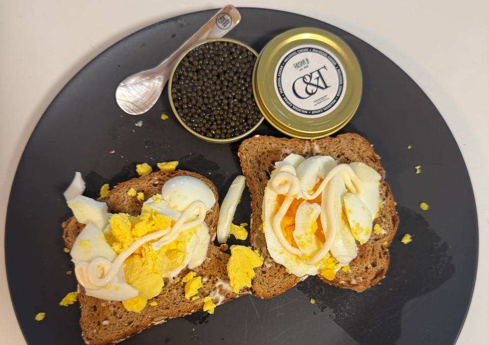 Toast with egg and caviar on a black plate beside an open tin